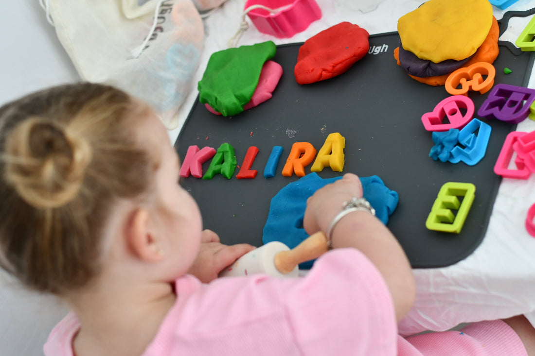 Child using colourful letter cutters and a rolling pin with Bio DoUgh on a play mat