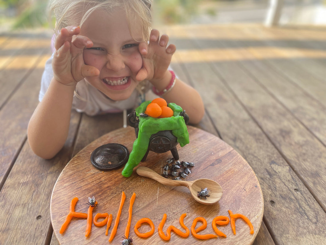 Smiling child with a green playdough cauldron and orange Halloween creation