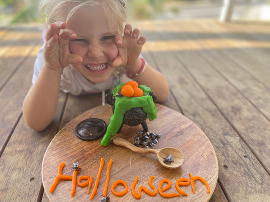 Smiling child with a green playdough cauldron and orange Halloween creation