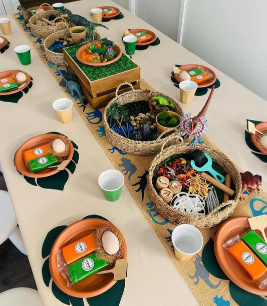 Dinosaur-themed party table set with colourful Bio DoUgh party favours and sensory play baskets