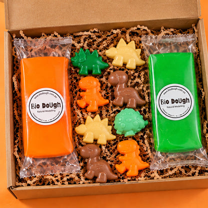a close up of a dinosaur playdough kit with orange and green playdough pouches and dinosaur figurines in yellow, brown, green and aqua.